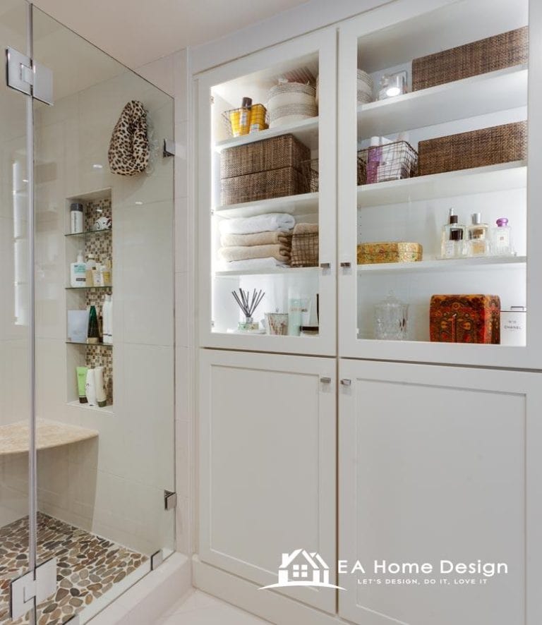 Luxurious walk-in glass shower with pebble tile floor and built-in seating at EA Home Design