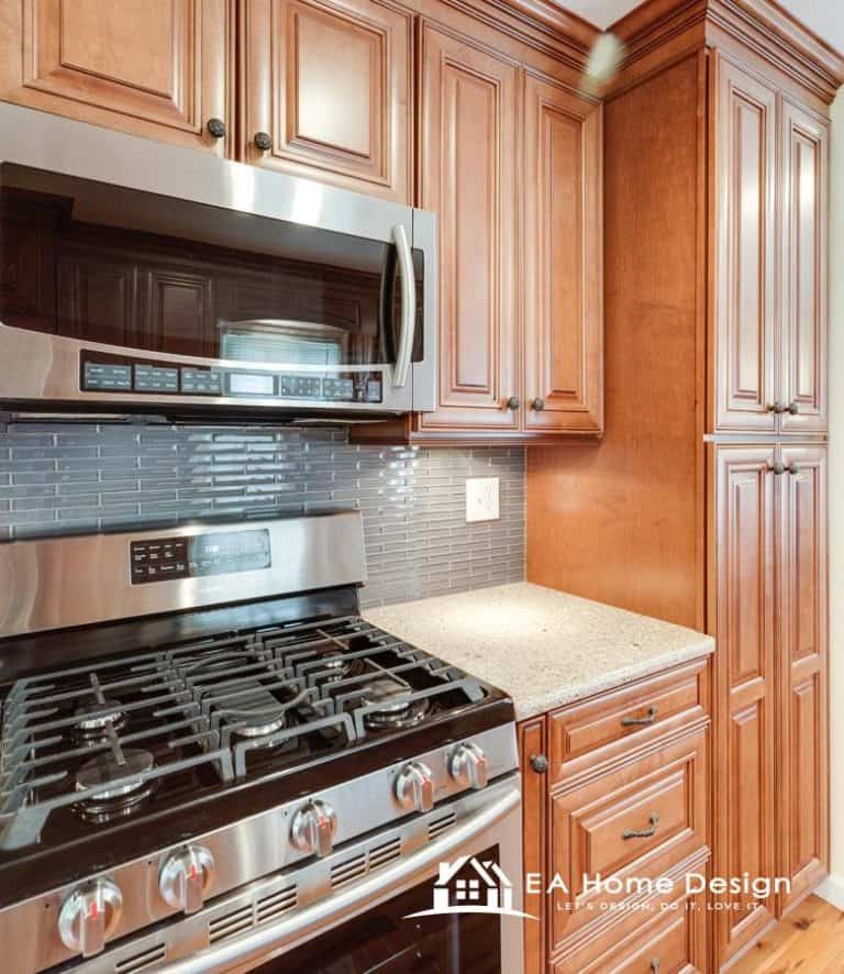 A wide-angle interior view of a home's kitchen and dining area. The space has rich, wood flooring and matching dark wood cabinetry. The left side features a large bay window, and a white door leading to another room is on the right.