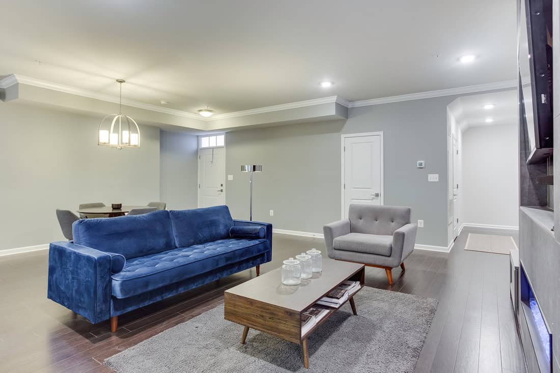 Living room designed by EA Home Design with navy velvet sofa, grey armchair, walnut coffee table and recessed lighting