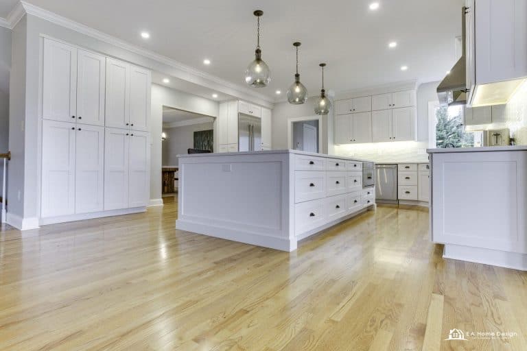Modern kitchen with island, metal stools, white cabinets, and lighting.