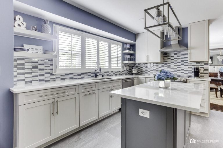 Modern kitchen with island, metal stools, white cabinets, and lighting.