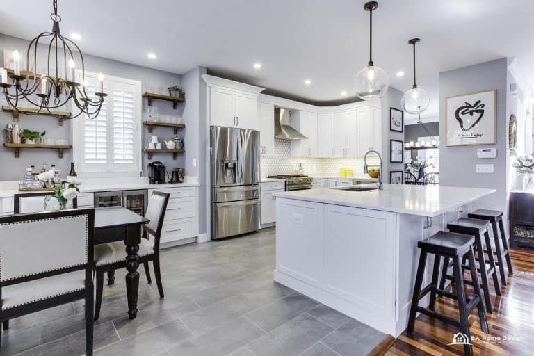 Modern kitchen with island, metal stools, white cabinets, and lighting.