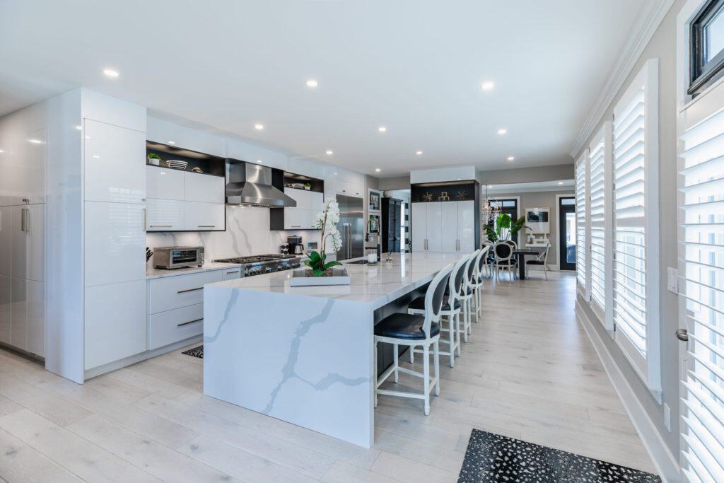 Bright modern kitchen with white cabinetry, marble island, and ample natural light from plantation shutters.