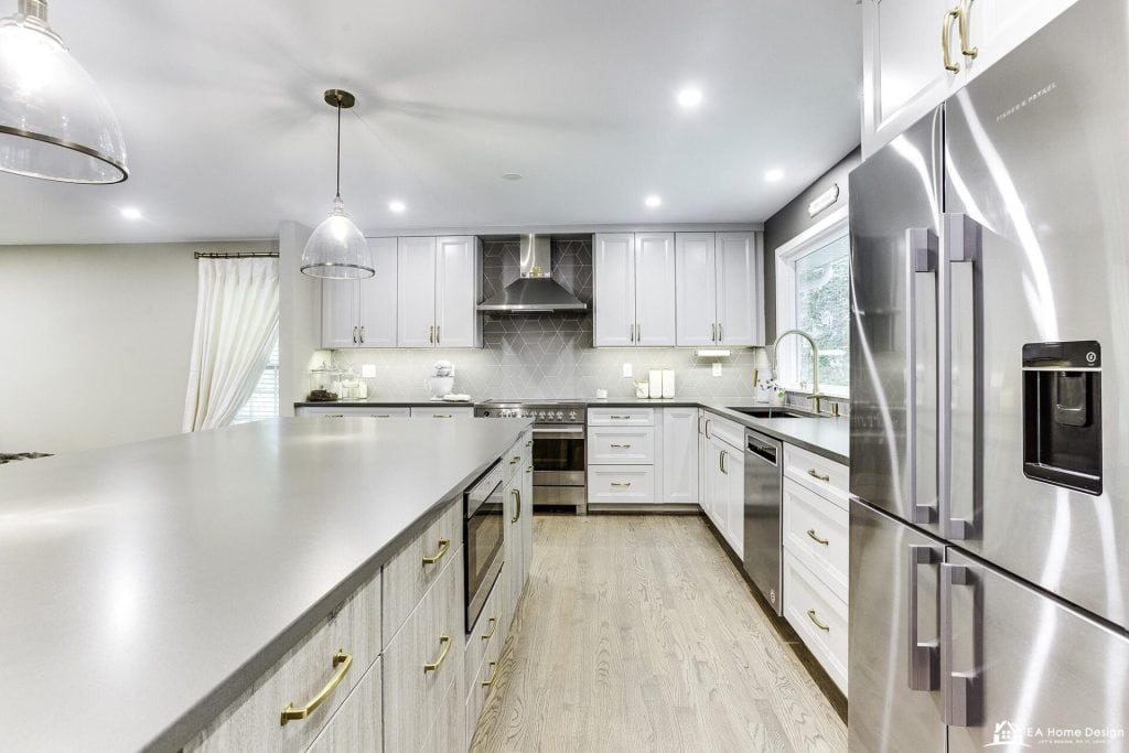 A view from the kitchen entrance showing a stainless steel fridge and stove, a central island with a sink, and beautiful track lighting.