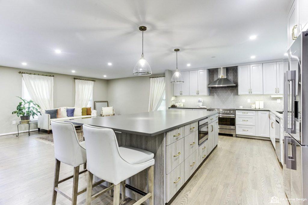 A wide view of a modern kitchen with sleek appliances, a large dining table, a sink under a window, and recessed ceiling lights.