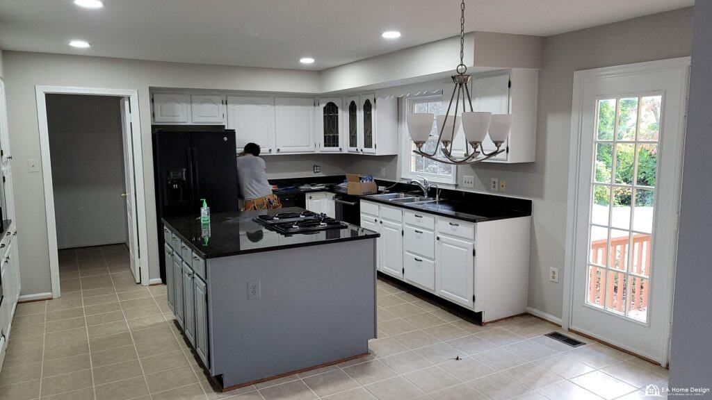 Modern white and black kitchen with an island, large window, and sliding glass door, ideal for home cooking and entertaining.