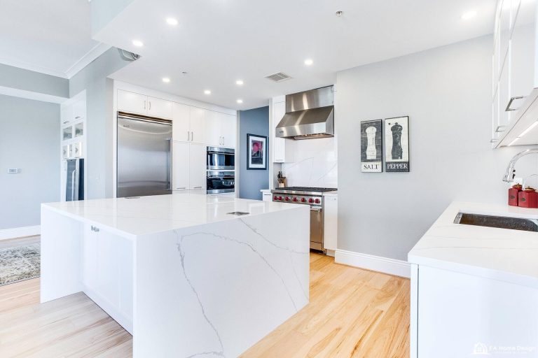 A modern kitchen from the dining area, showcasing a large fridge, a gas stove, a farmhouse sink, and elegant light fixtures.