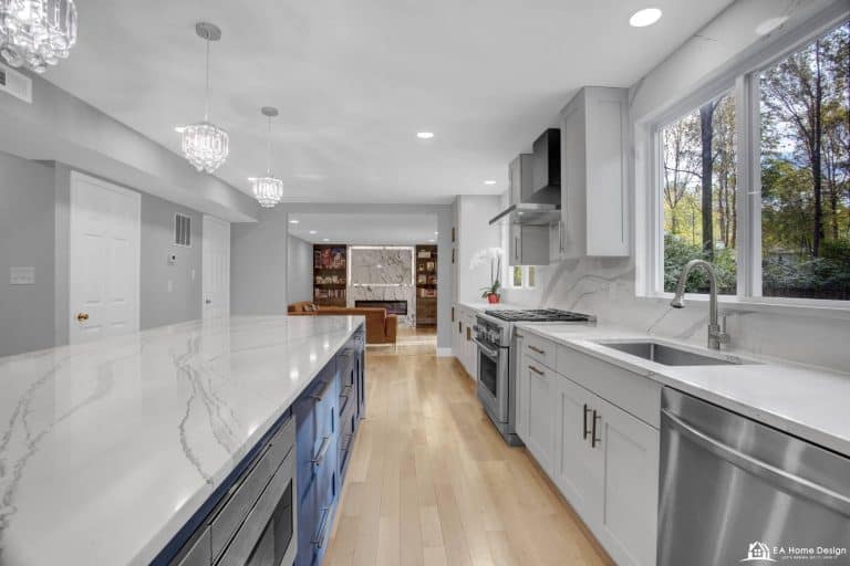 Bright modern kitchen with white marble countertops and large window overlooking trees