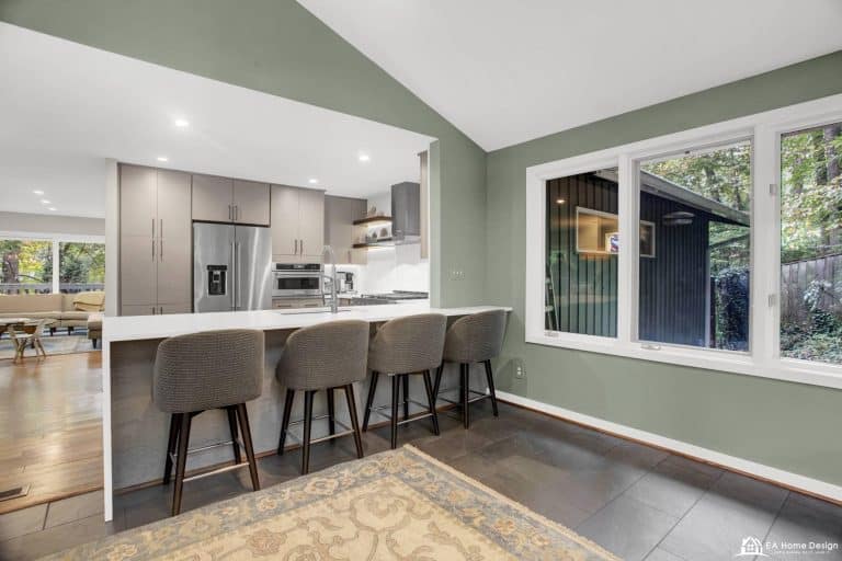 A close-up of a kitchen sink with visible pipes, surrounded by a clean counter, with a glimpse of a modern stove and fridge in the background.