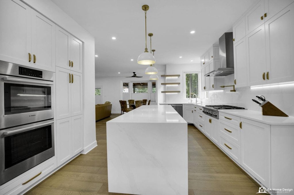 Bright white modern kitchen with gold accents, spacious island, stainless steel appliances, and large windows.