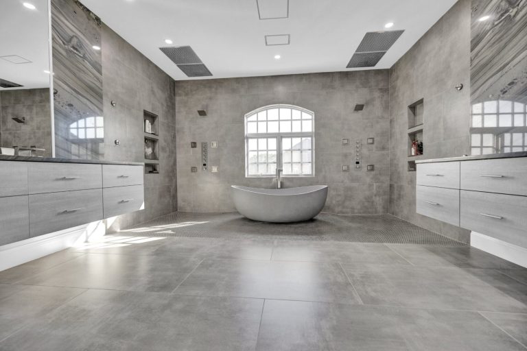 After: freestanding tub under the arched window, floating vanities and curbless shower zones either side