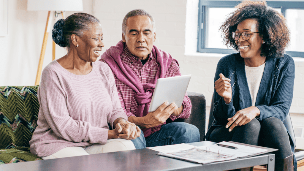 Three people on a couch with tablet, papers, and pens in a living room.