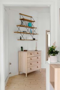 Light wood dresser under three shelves creates a clever closet conversion in a bright, white bedroom.