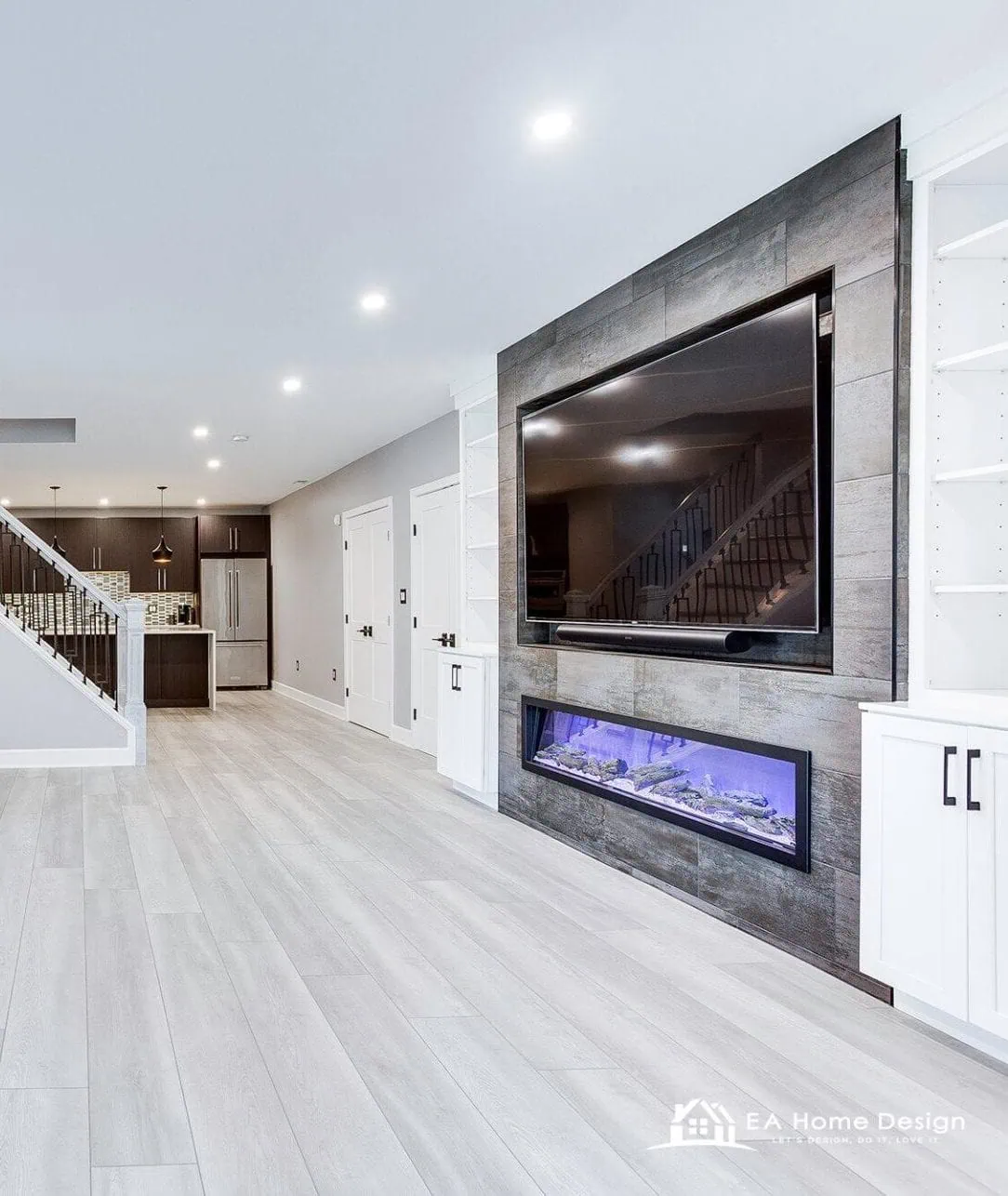 Finished basement family room in Northern Virginia with a wall mounted television on a stone feature wall, an electric fireplace and white built-in cabinets