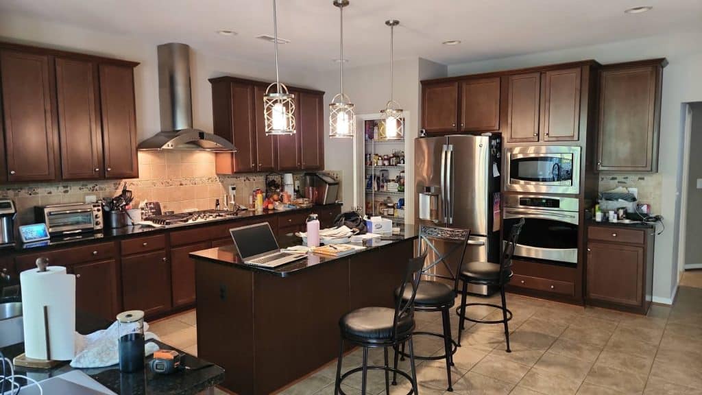 A full view of a spacious kitchen with a dining island, a built-in fridge, and a professional-grade stove, all illuminated by stylish overhead lighting.