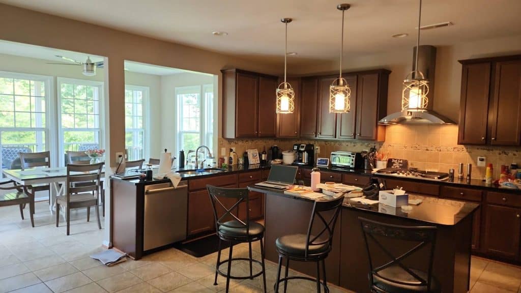 A full view of a spacious kitchen with a dining island, a built-in fridge, and a professional-grade stove, all illuminated by stylish overhead lighting.