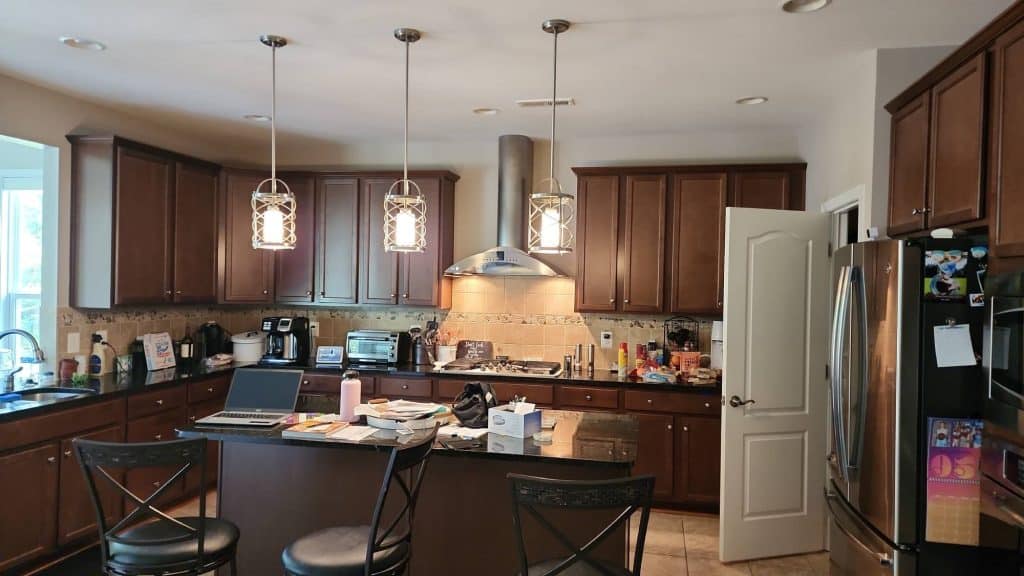 A full view of a spacious kitchen with a dining island, a built-in fridge, and a professional-grade stove, all illuminated by stylish overhead lighting.