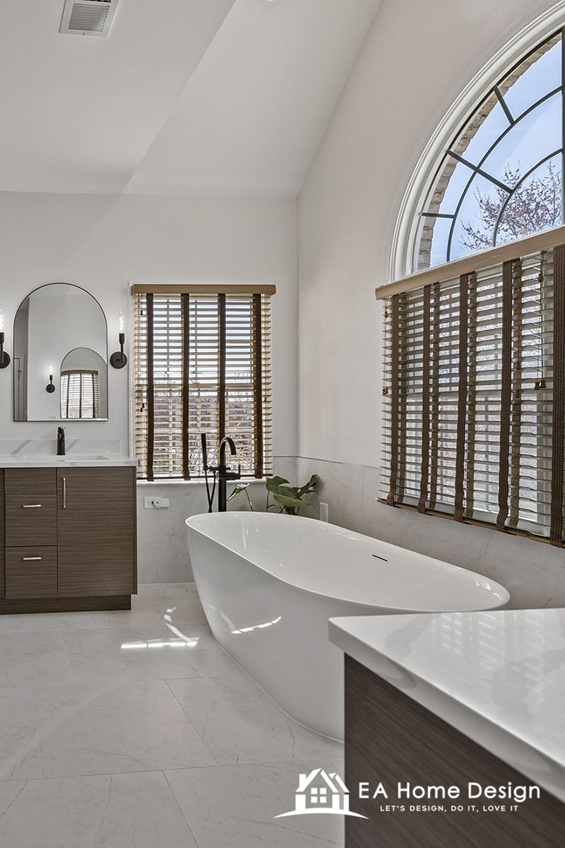 Bathroom with a freestanding tub, a dark wood double vanity, large format light tile floor and a tall arched window