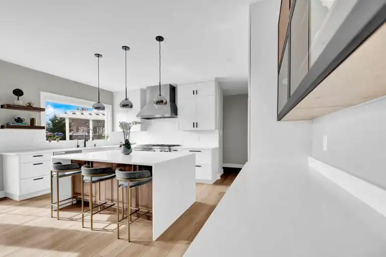 Modern kitchen with white island, pendant lights, bar stools, white cabinets, and stainless steel appliances.