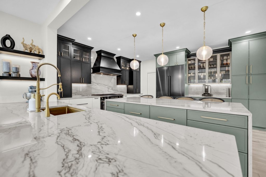 After: the quartzite waterfall island with brass pendants and the green cabinet wall