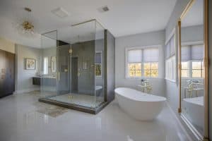 Luxurious modern bathroom with freestanding bathtub and glass-enclosed shower, featuring elegant gold accents and natural light.