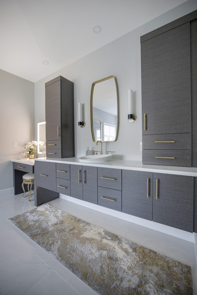 After: floating gray oak vanity with a lowered makeup counter, tall linen cabinets and gold sconces