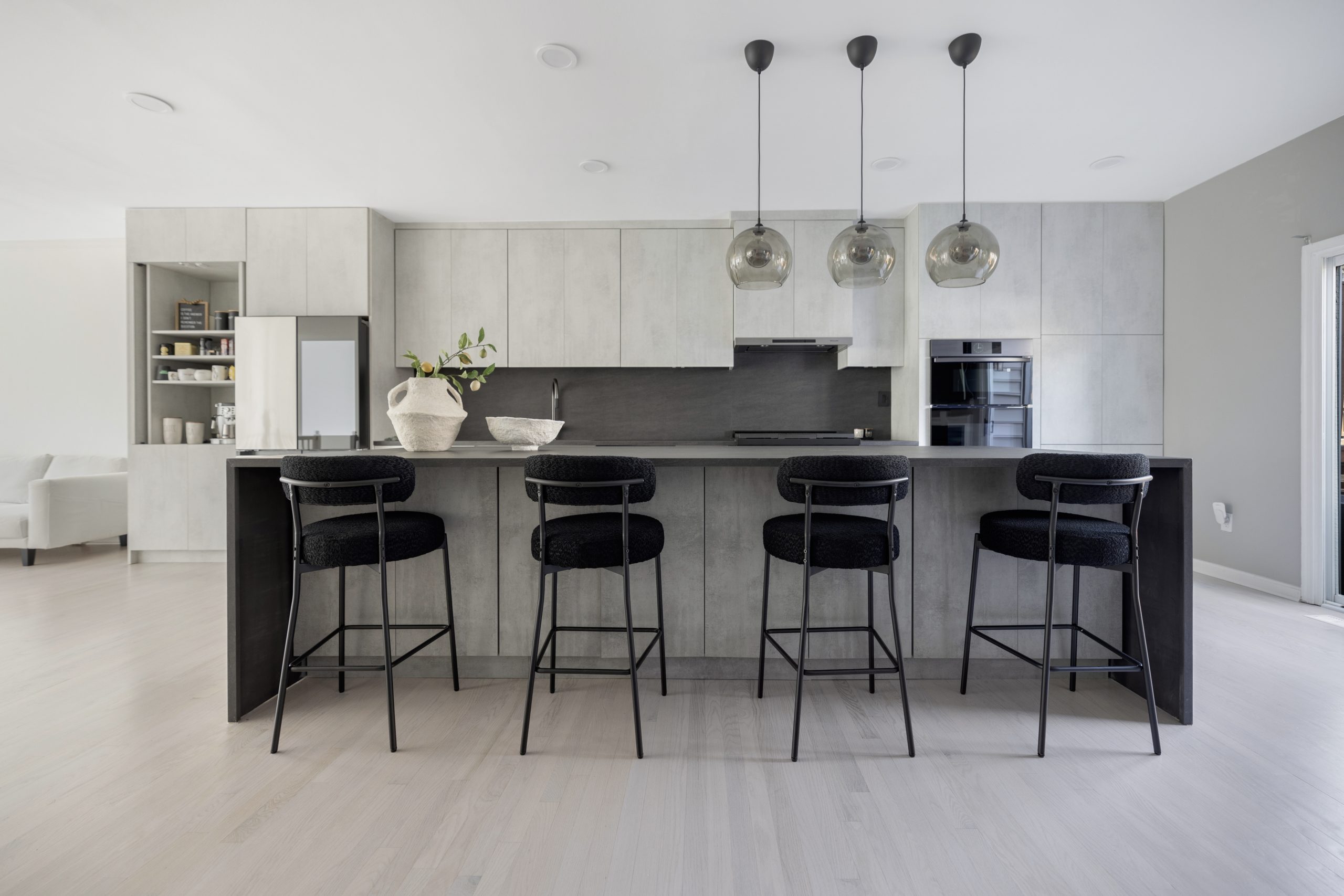 Sleek modern kitchen with minimalist design, black bar stools, pendant lighting, and light grey cabinetry.