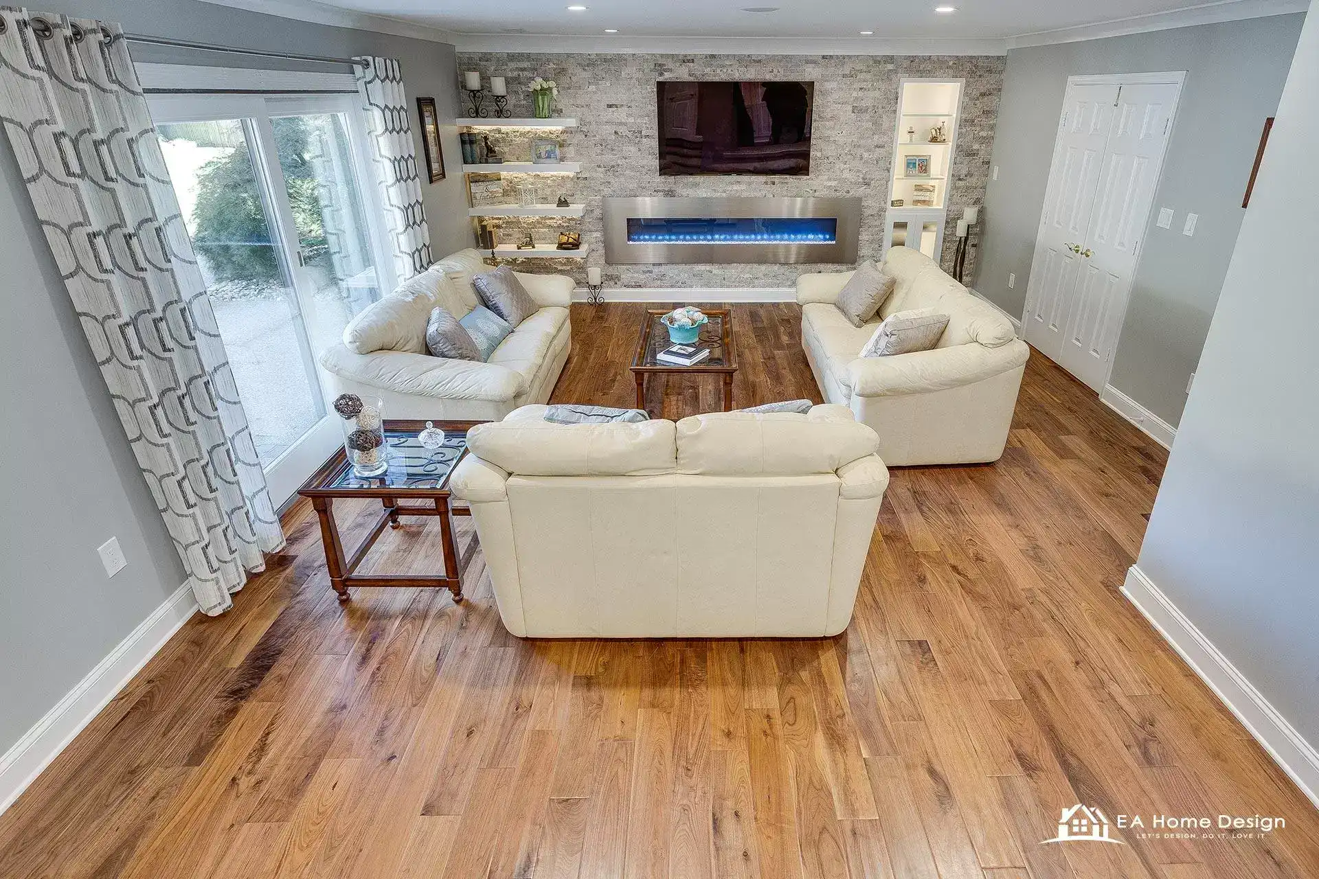 Living room with a floor to ceiling stone fireplace wall, white sectional sofas and wide plank hardwood floors