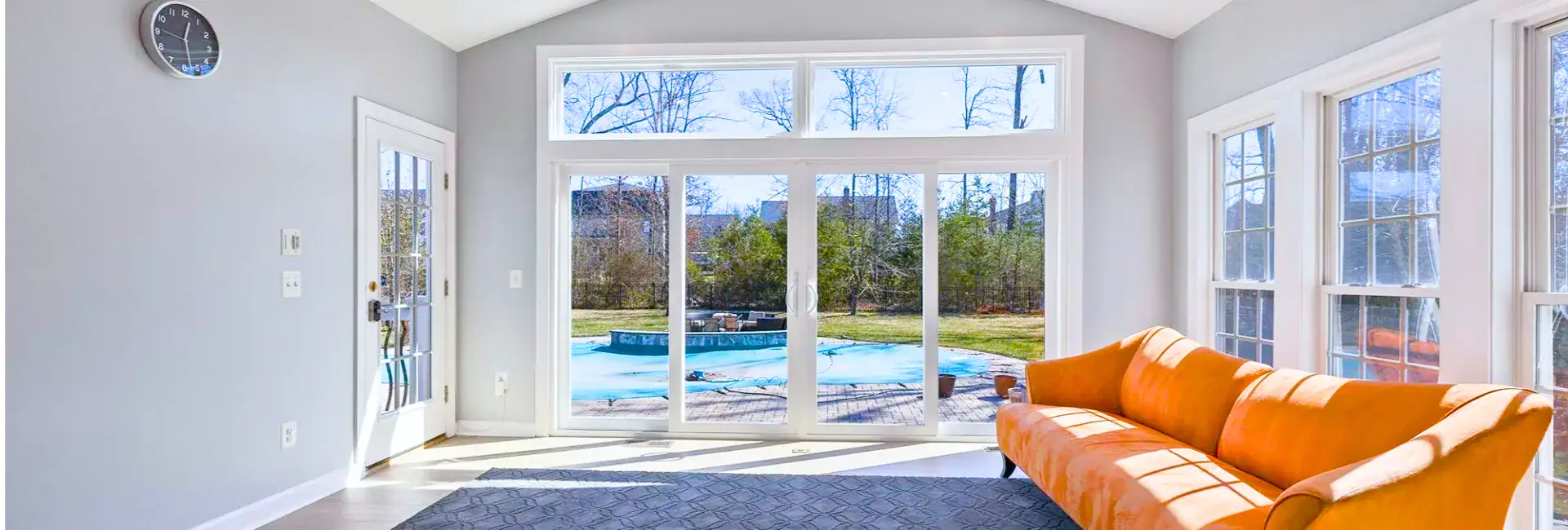 Sunroom addition with a wall of windows and glass doors to a pool, an orange sofa and a dark rug on a hardwood floor