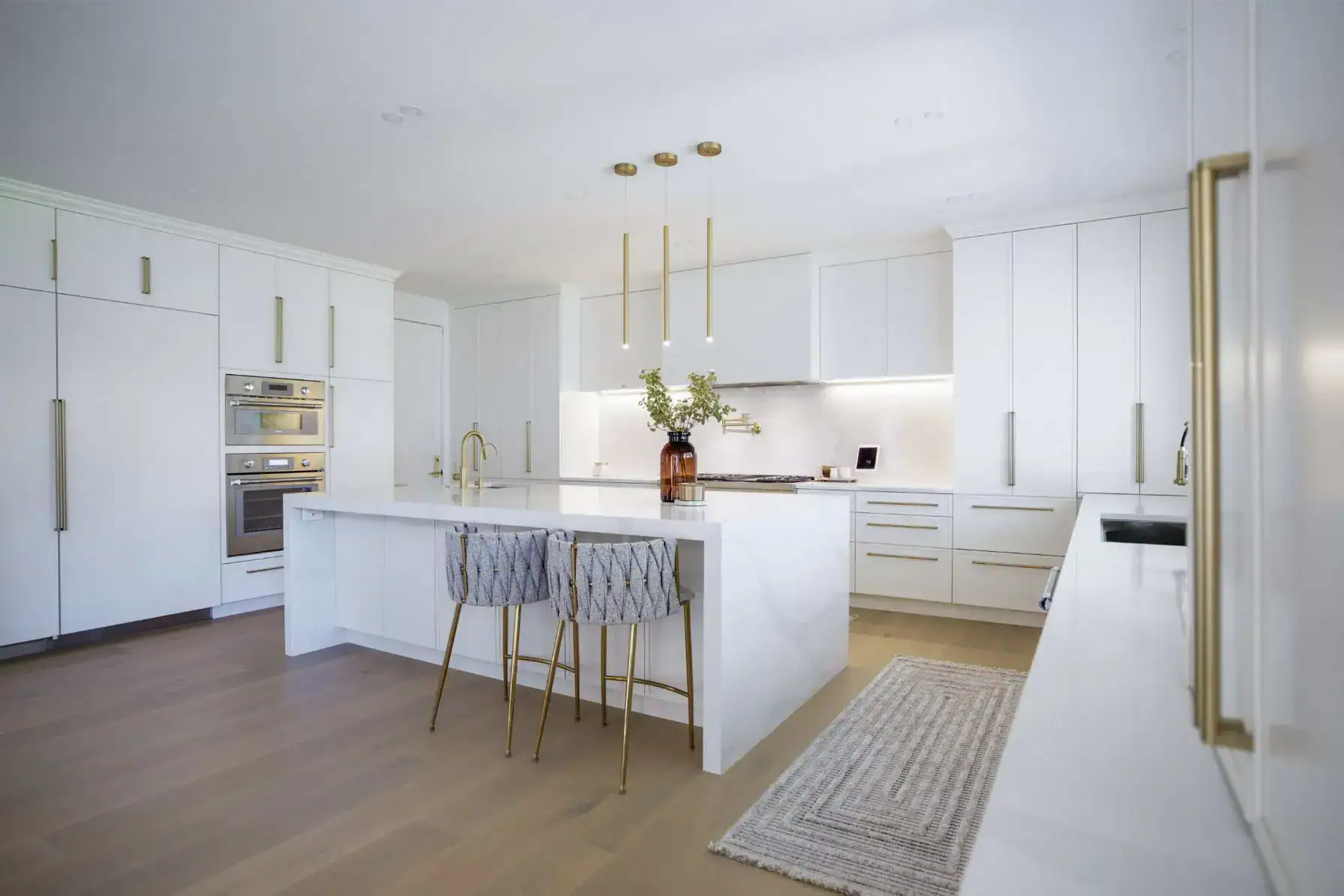 All white kitchen with a marble island, brass hardware and white oak floors