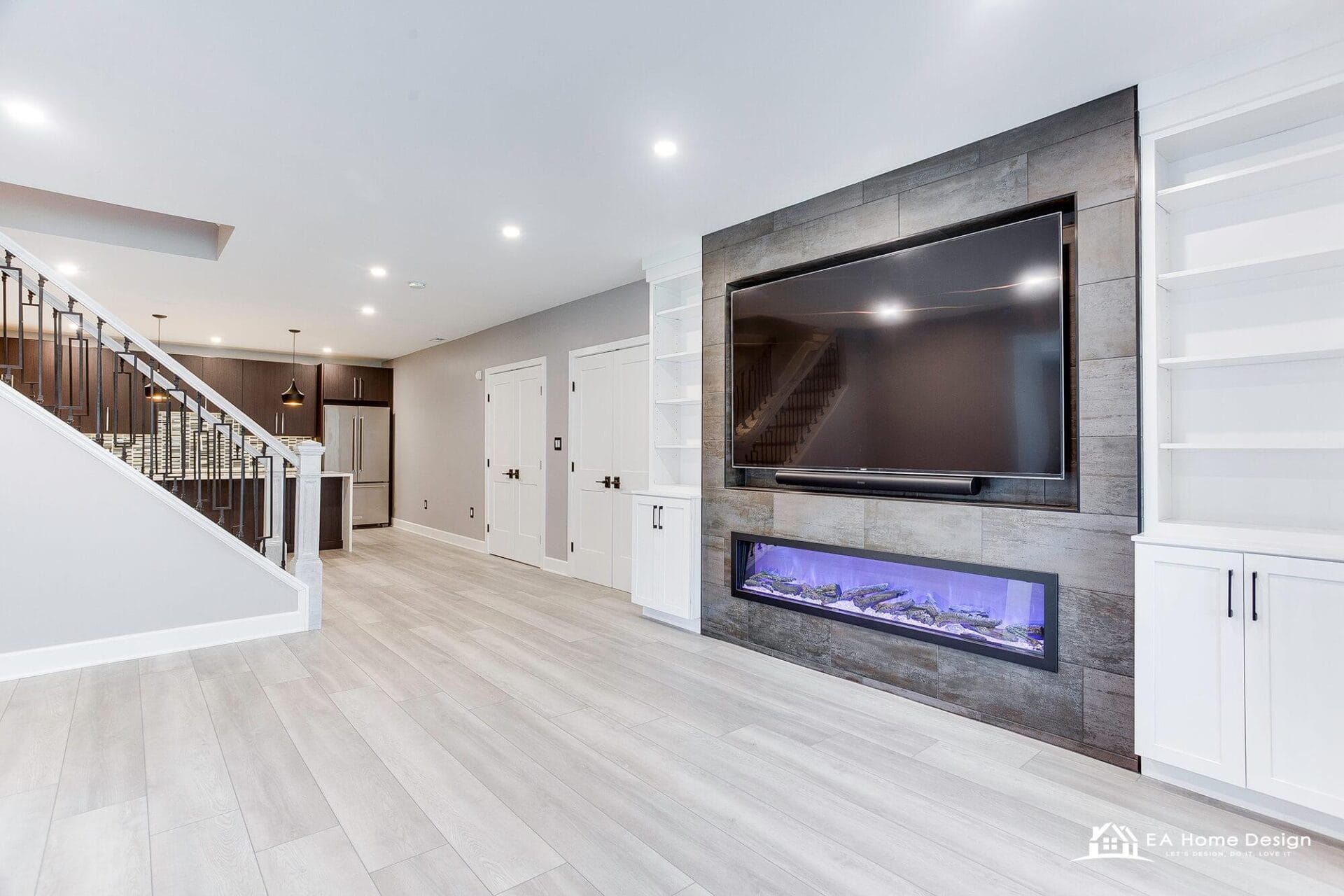 Finished basement by EA Home Design: media wall with a linear fireplace and built-ins, the stair and the kitchenette beyond