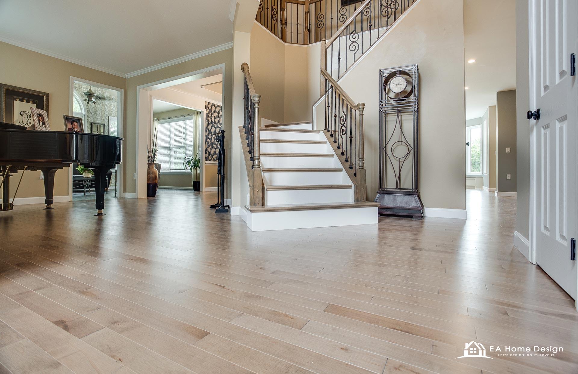 Foyer in a Northern Virginia home with light maple flooring running continuously into the living room with a grand piano and a curved staircase