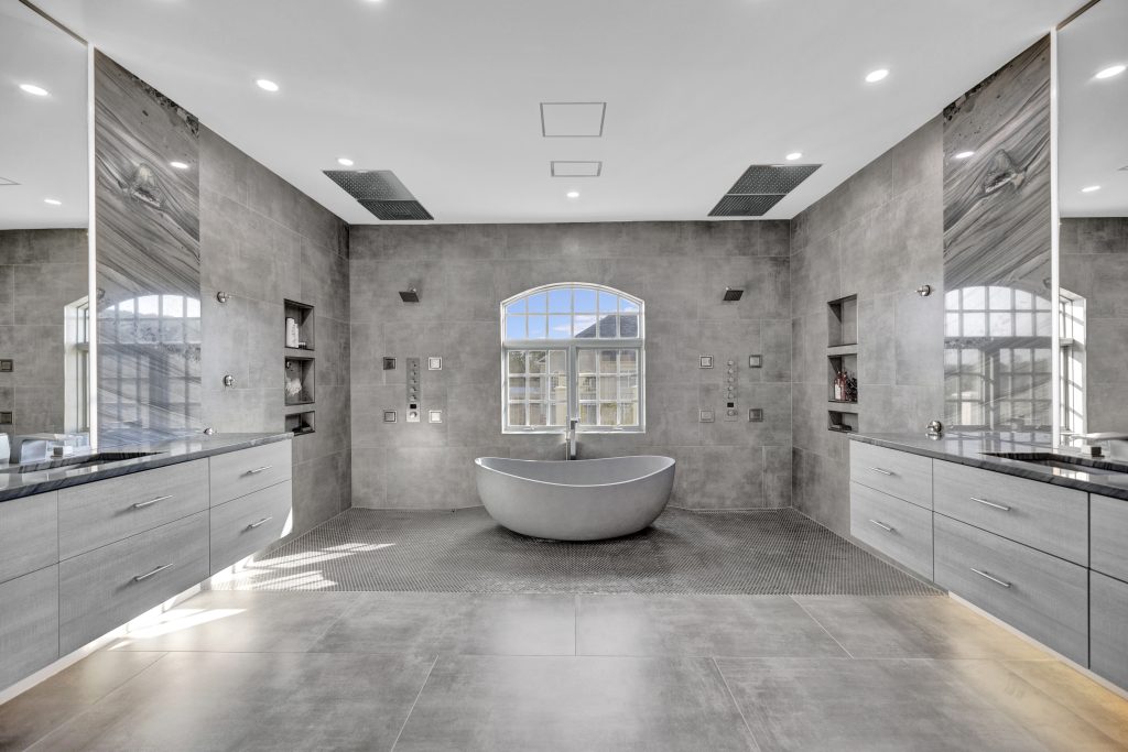 Modern luxury bathroom with freestanding bathtub and gray tiled walls and floors.