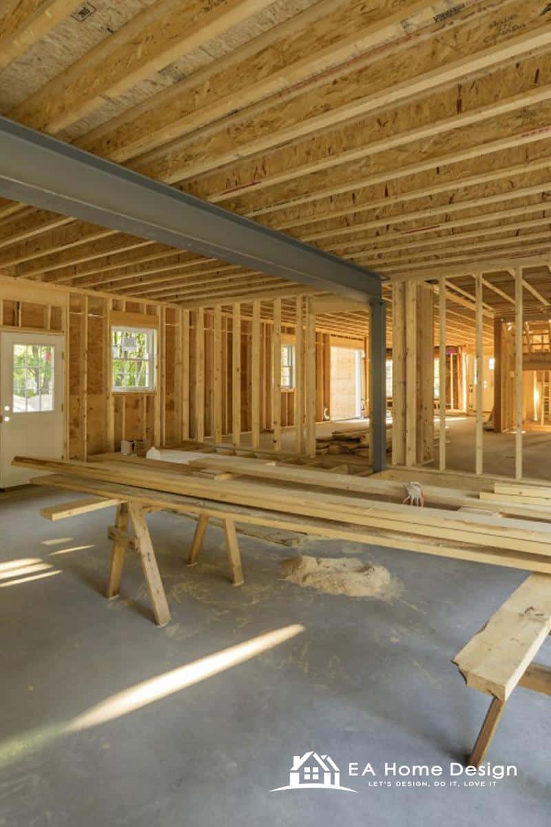 Workmen installing a cardboard wall panel using a ladder, with tools and construction materials visible in the workspace.