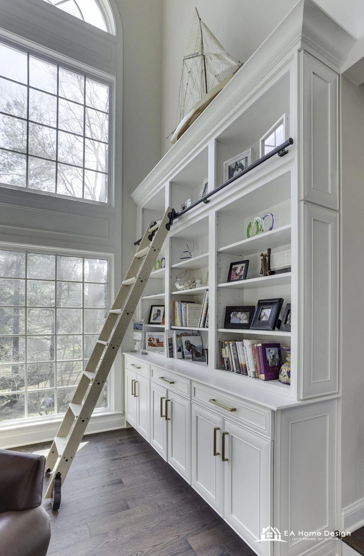 Floor to ceiling white built-in bookcases with a rolling library ladder beside a tall window