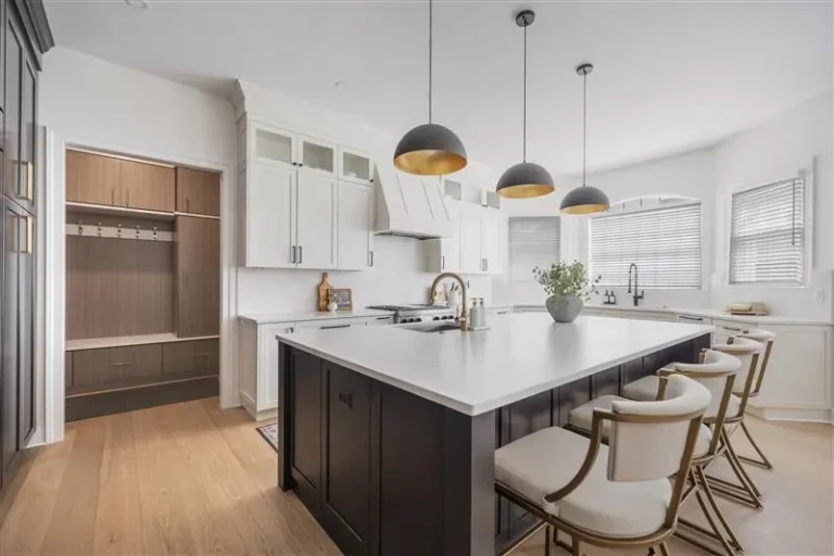 Modern kitchen with white cabinets and black island, bright natural light from windows, stylish pendant lighting.