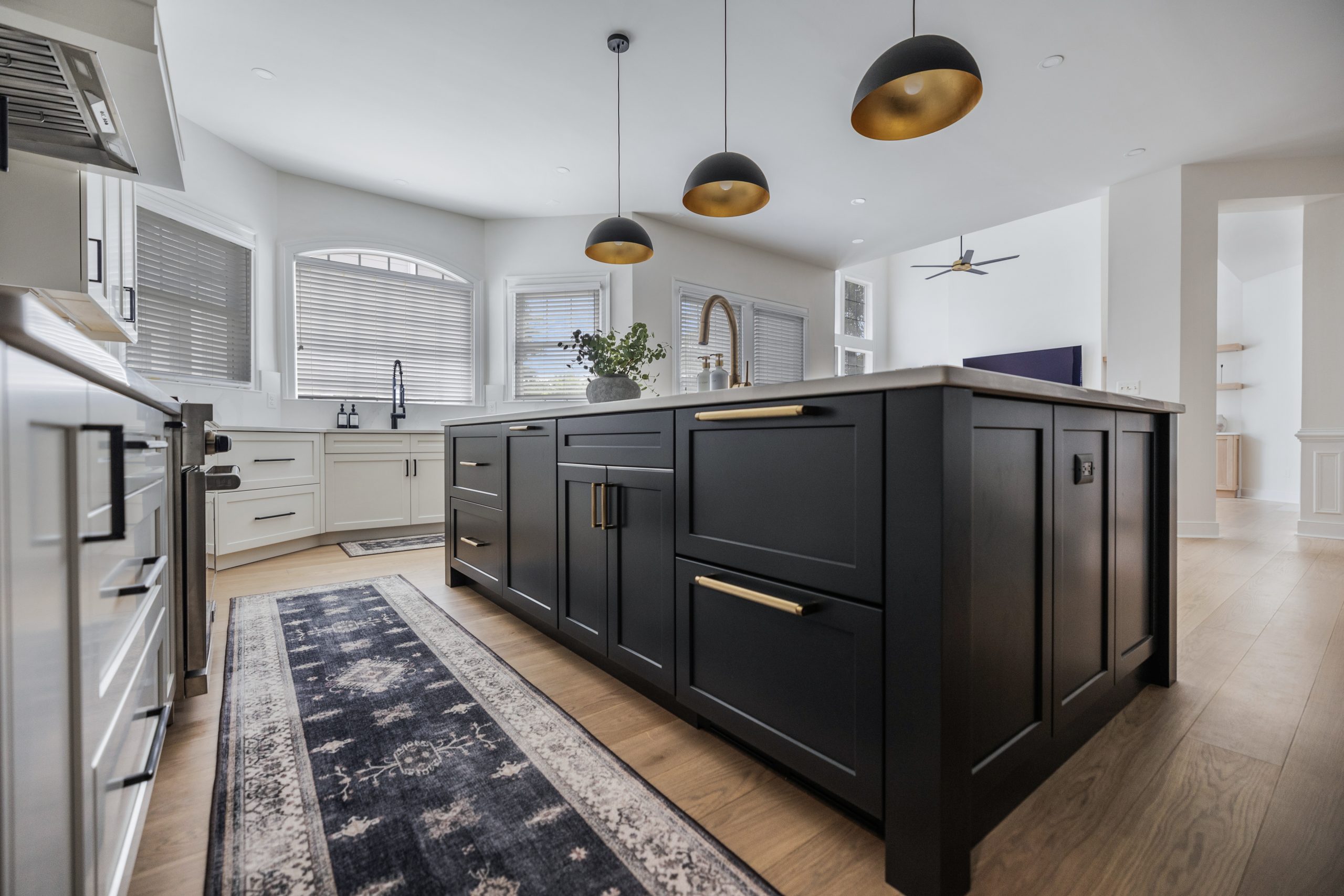 black kitchen island with gold handles and faucet, modern open-concept kitchen and living space, natural light, contemporary home design