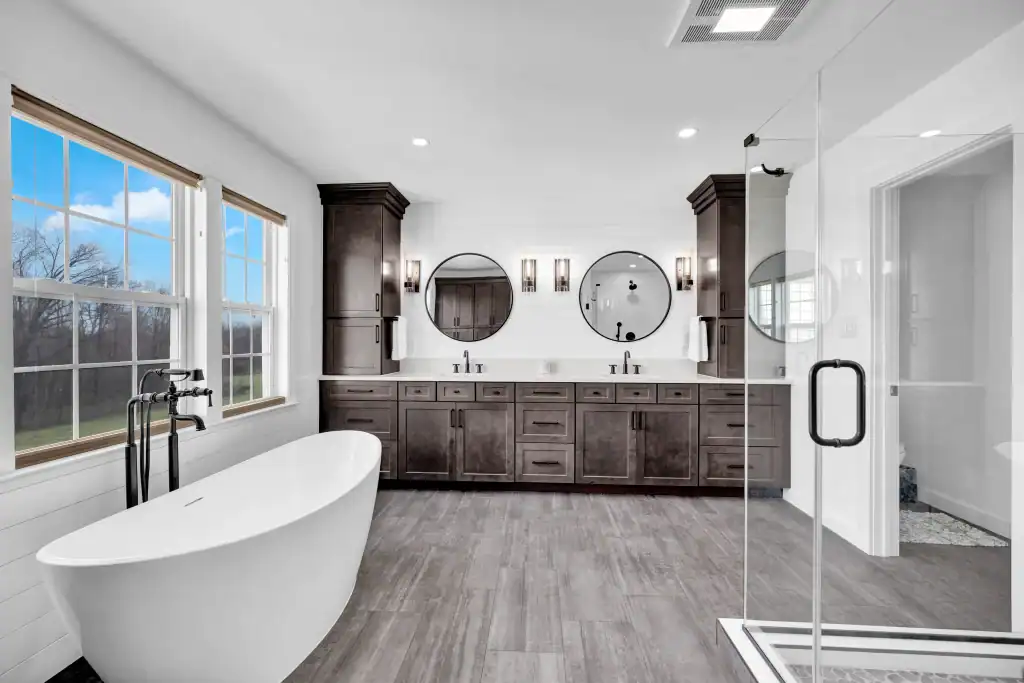 Modern bathroom with freestanding bathtub, double vanity, and walk-in glass shower, featuring sleek dark wood cabinetry and large windows for natural light.