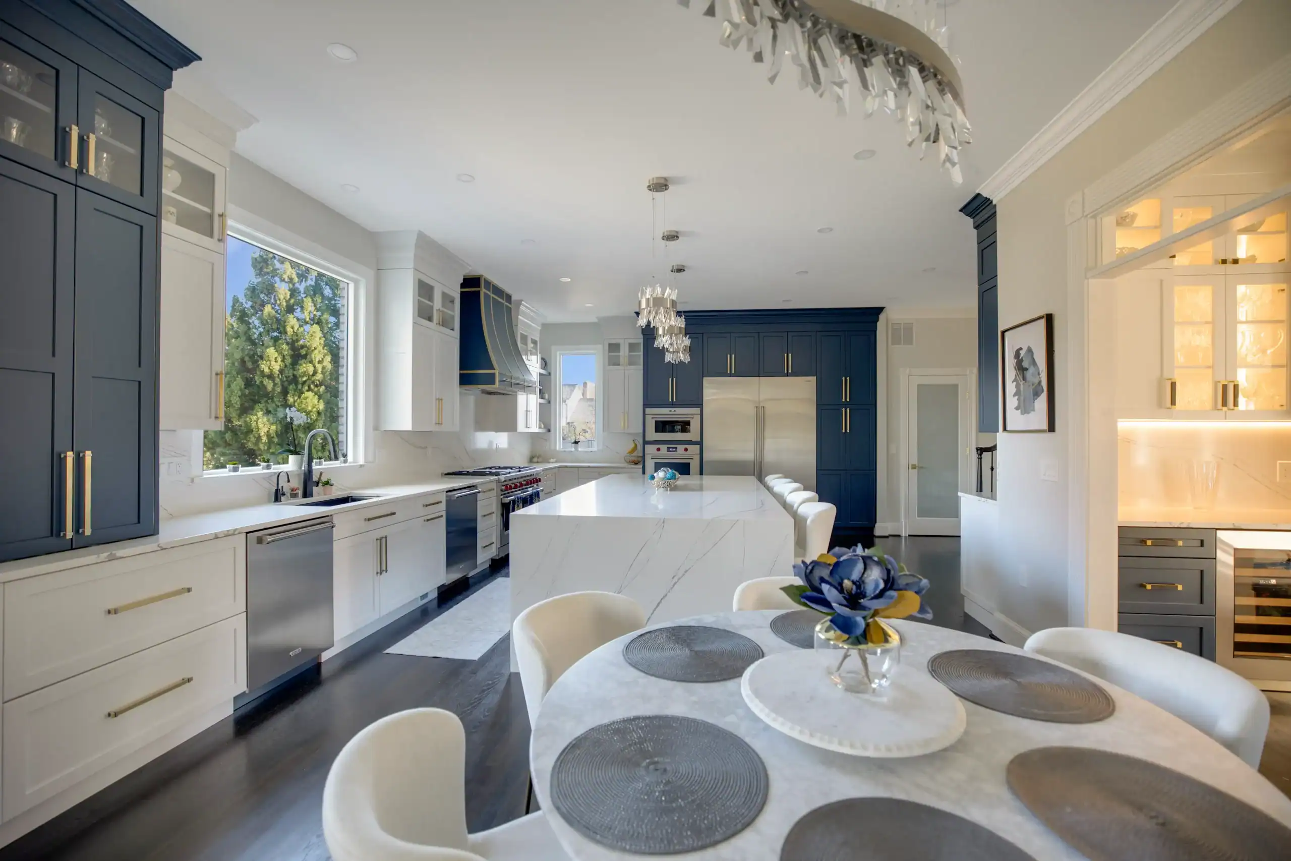 Modern kitchen with navy and white cabinetry, marble island, and elegant lighting fixtures.