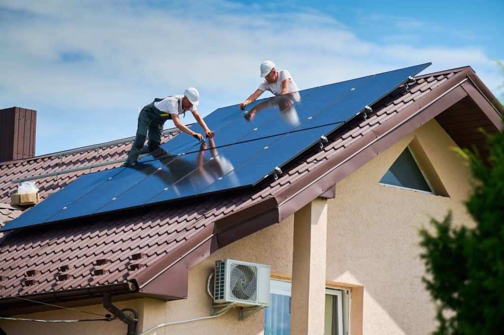 Solar panel installation on residential roof by two workers.