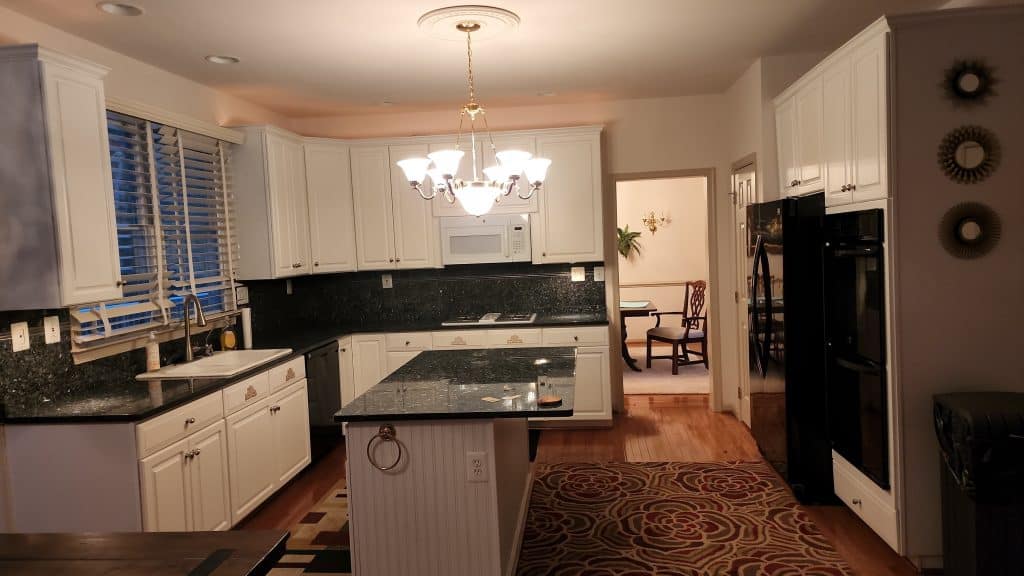 Modern white kitchen with black granite countertops and elegant chandelier lighting.