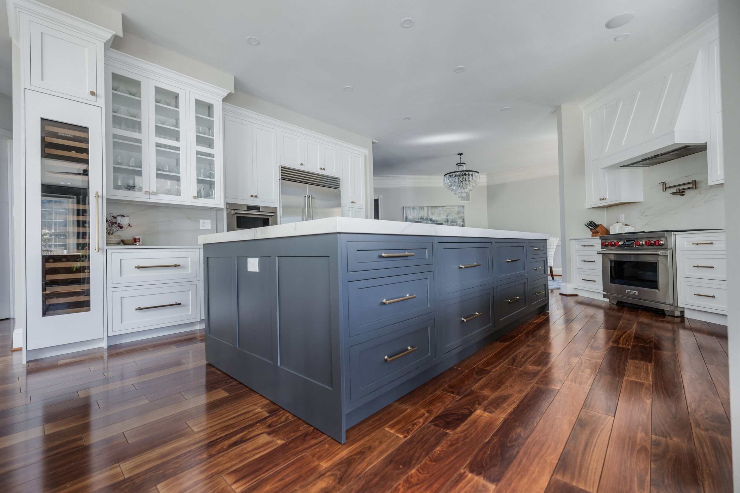Luxury modern kitchen with blue island and white cabinetry, hardwood flooring, and stainless steel appliances.