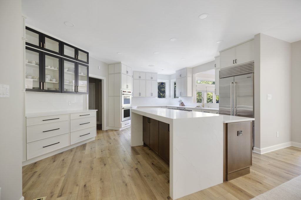 Spacious modern kitchen with white cabinetry, glass-front upper cabinets, a large island, built-in appliances, and large windows—perfect for your next home improvement Fairfax County, VA project.