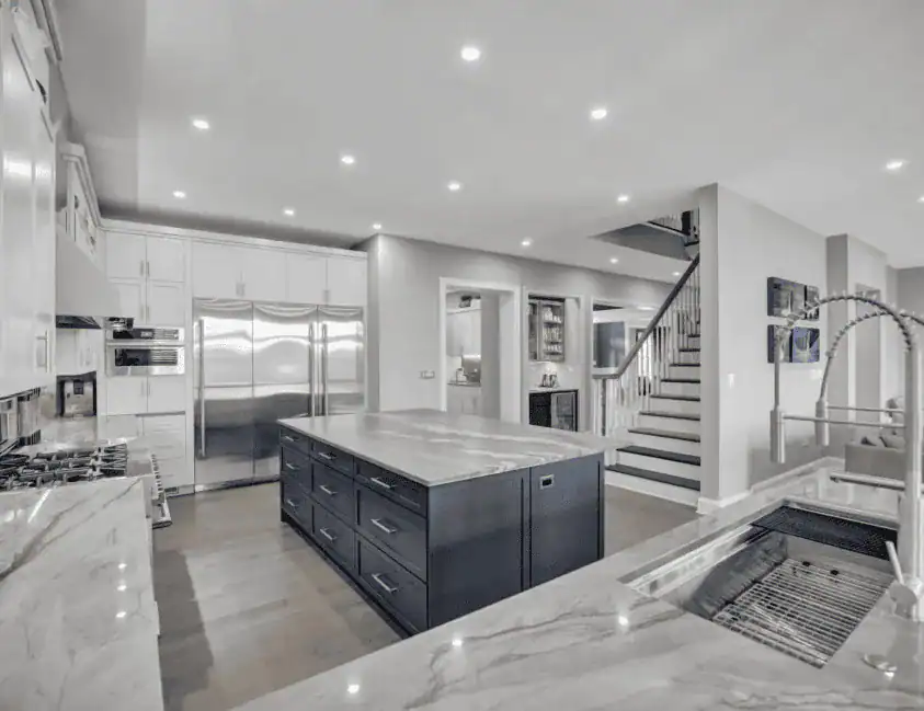 Modern kitchen with marble countertops, a large central island, stainless steel appliances, sleek cabinetry, and a spiral spring faucet—perfect for home improvement in Fairfax County, VA—with a staircase and hallway visible in the background.