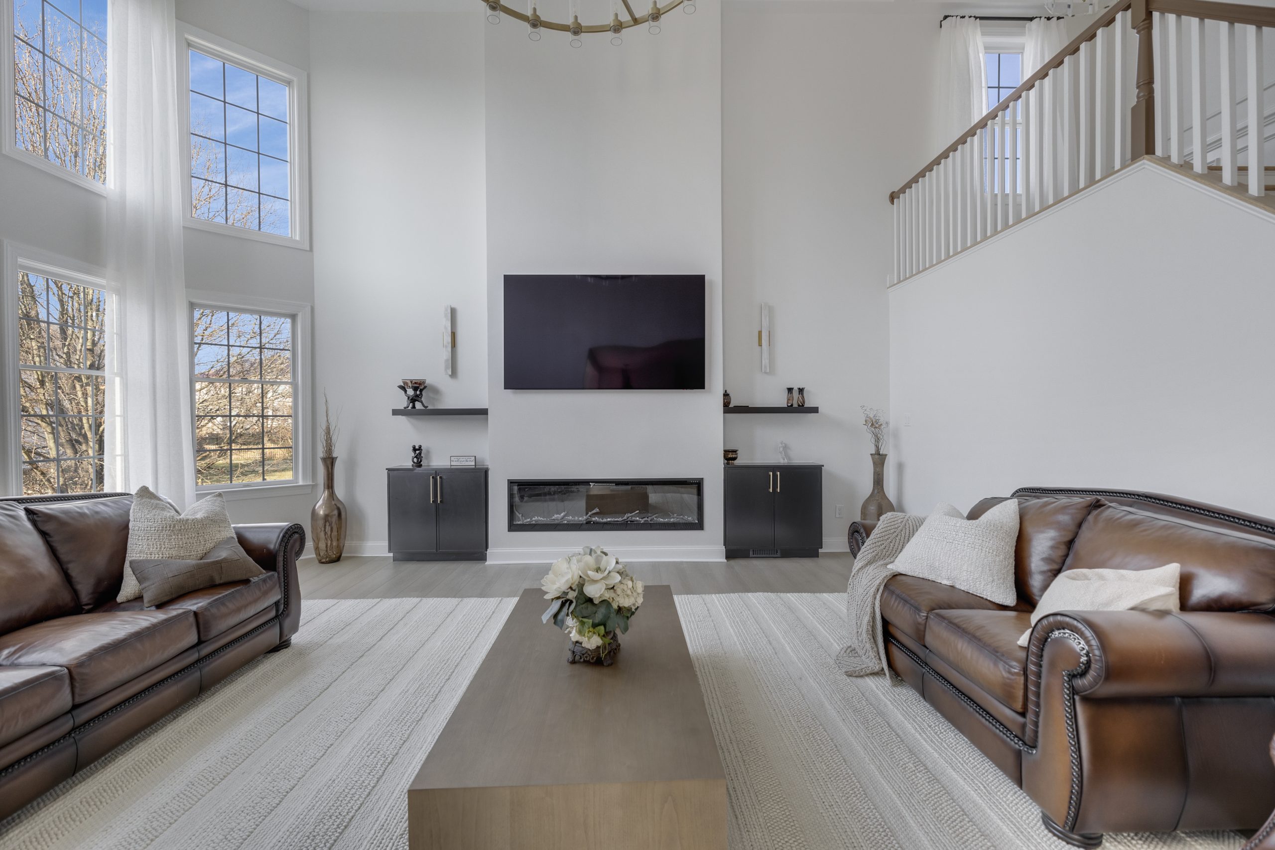 Bright two story family room in Northern Virginia with leather sofas, a linear fireplace and wall mounted television