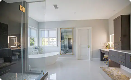 Modern bathroom with a freestanding bathtub, glass-enclosed shower, double sink vanity with lighted mirrors, and natural light from large windows; neutral tones and elegant decor throughout.