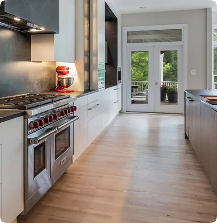 Modern kitchen with light wood floors, white cabinets, stainless steel appliances, a red stand mixer, and large glass doors leading to a green outdoor area.
