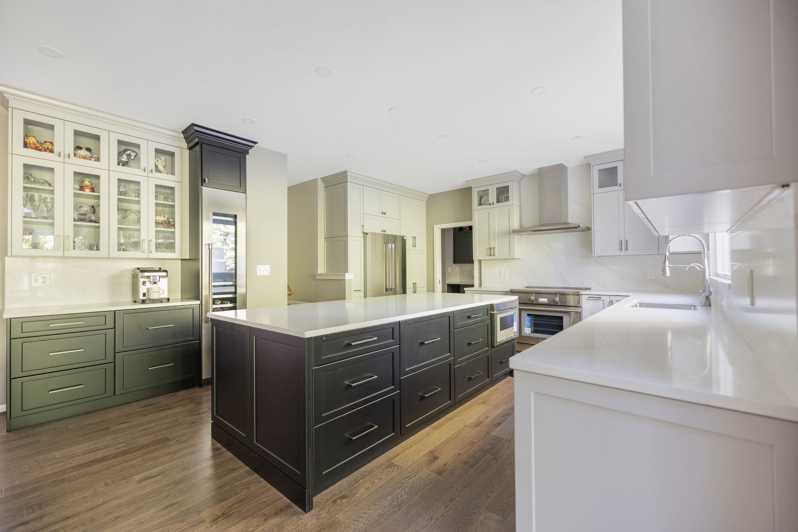 Transitional kitchen in Northern Virginia by EA Home Design with sage green shaker perimeter cabinets, glass-front uppers, a dark stained island and white quartz counters