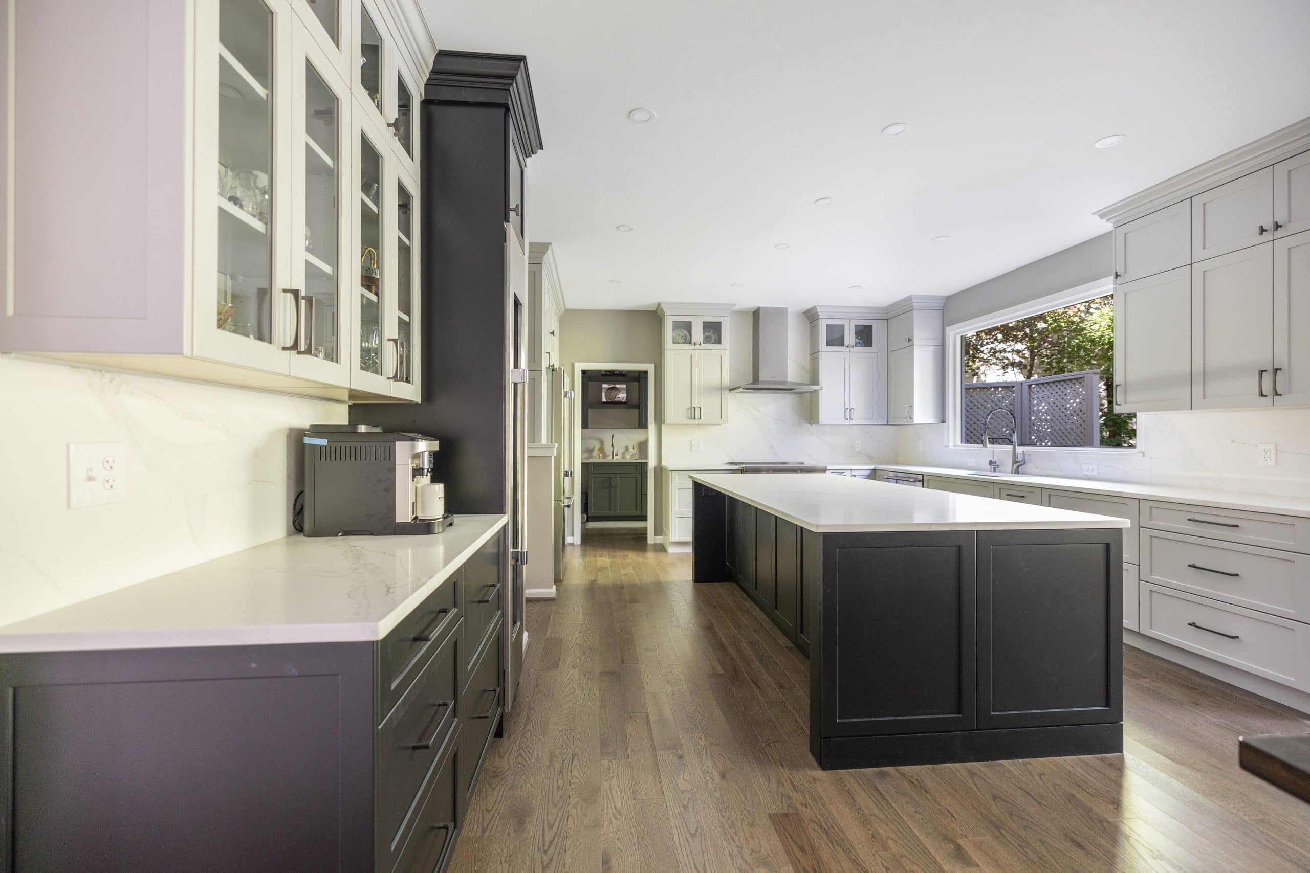 Charcoal kitchen island with white quartz top in an open Northern Virginia kitchen with glass front uppers and a wall hood