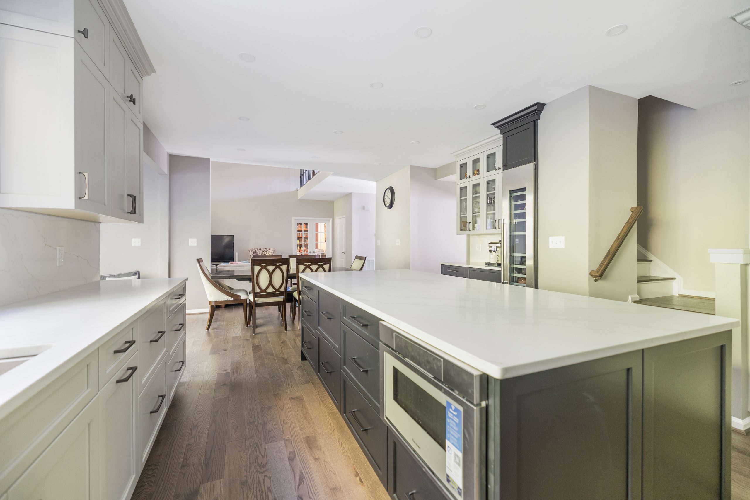 Long grey kitchen island in Northern Virginia with quartz top, built-in microwave drawer and seating, open to a dining area